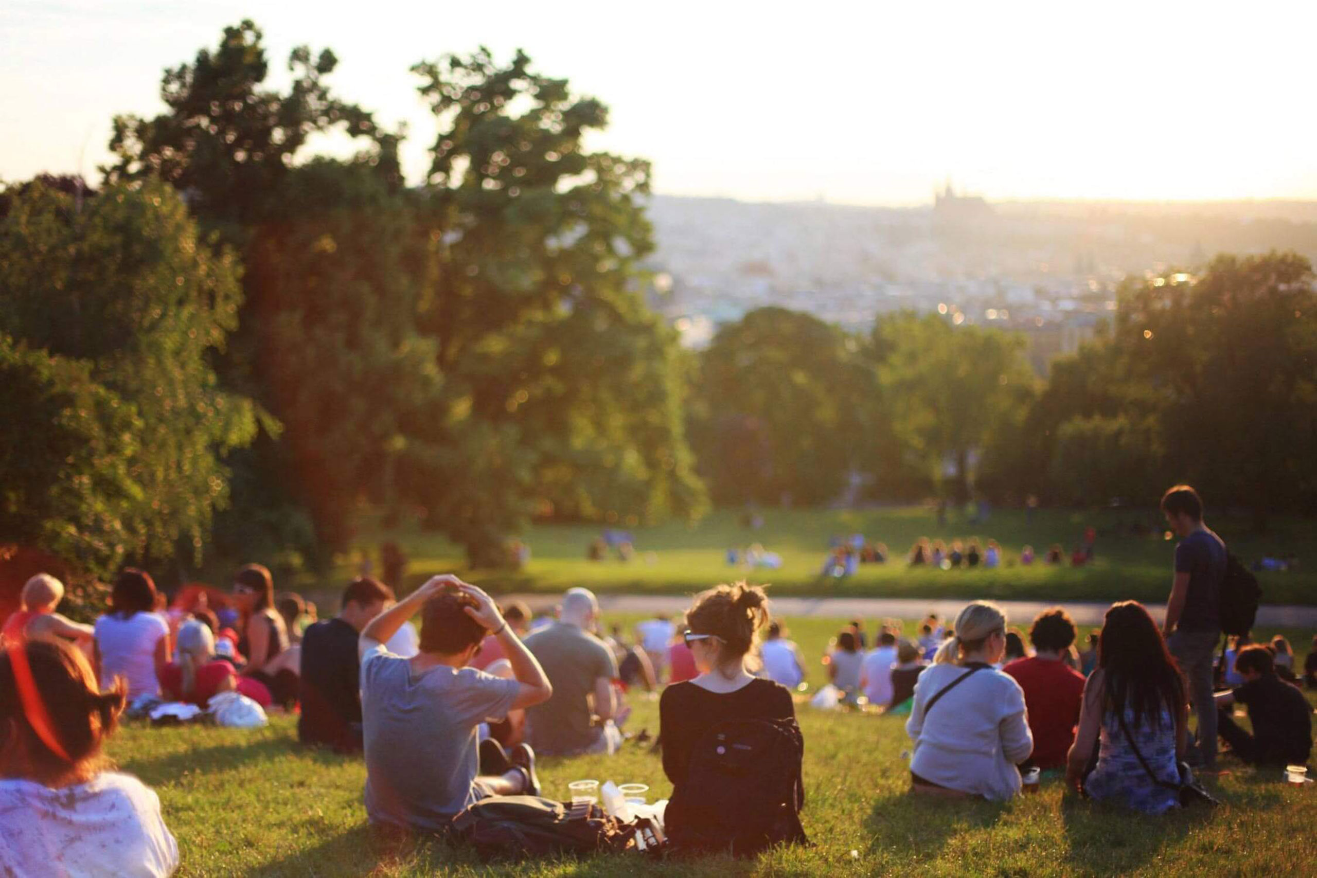 a group of people sat in a park watching the sun go down at sunset