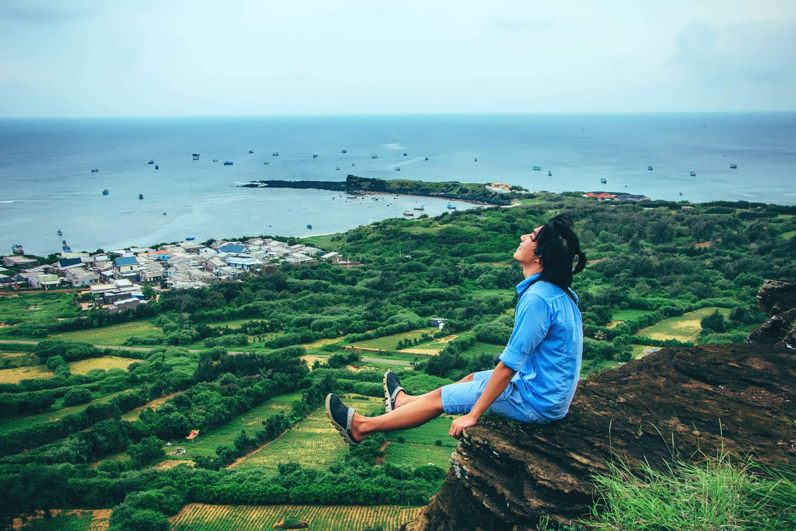 happy young woman sat on a cliff edge thinkinbg about her emergency loan